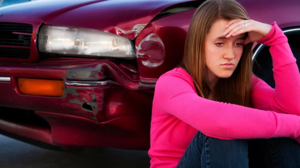 A woman looking stressed and sitting by her car after an accident. 